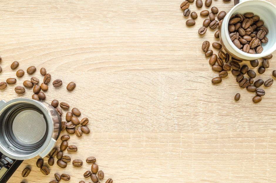 Coffee beans scattered around a tamper and cup on a wooden surface, perfect for caffeine lovers.